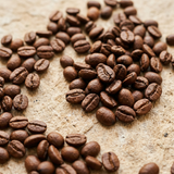 Close-up of medium-dark roasted coffee beans scattered on warm pale stone.