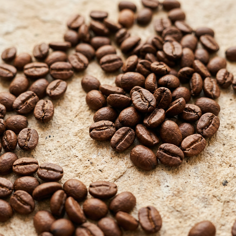 Close-up of medium-dark roasted coffee beans scattered on warm pale stone.