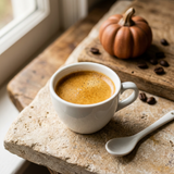 Espresso with golden crema in a white cup beside coffee beans and a decorative pumpkin.