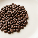 Medium-to-dark roasted whole coffee beans on a light background.