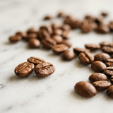Close-up of brown roasted coffee beans scattered on a pale stone surface.